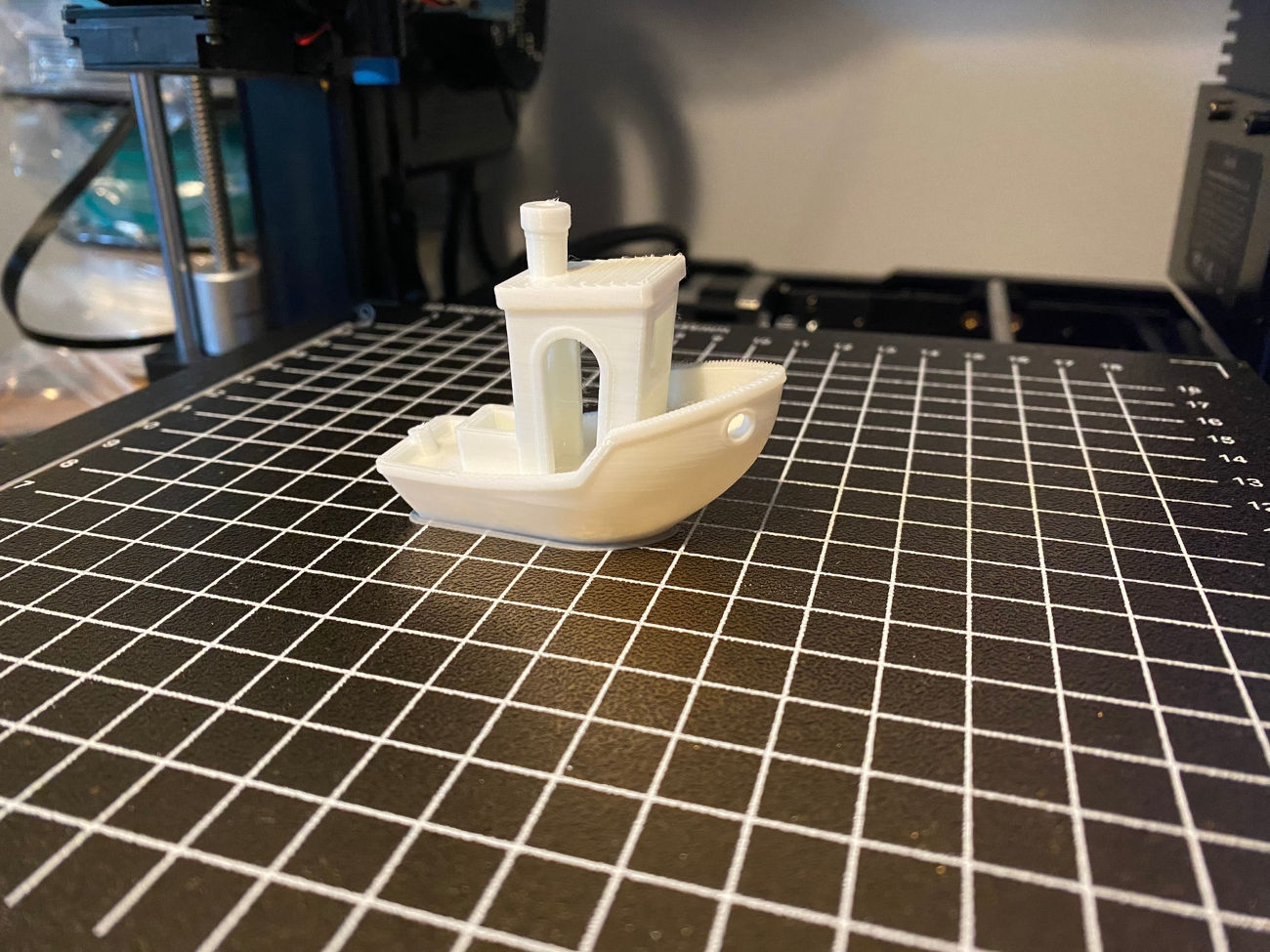 A white 'Benchy' sat on the 3D printer bed