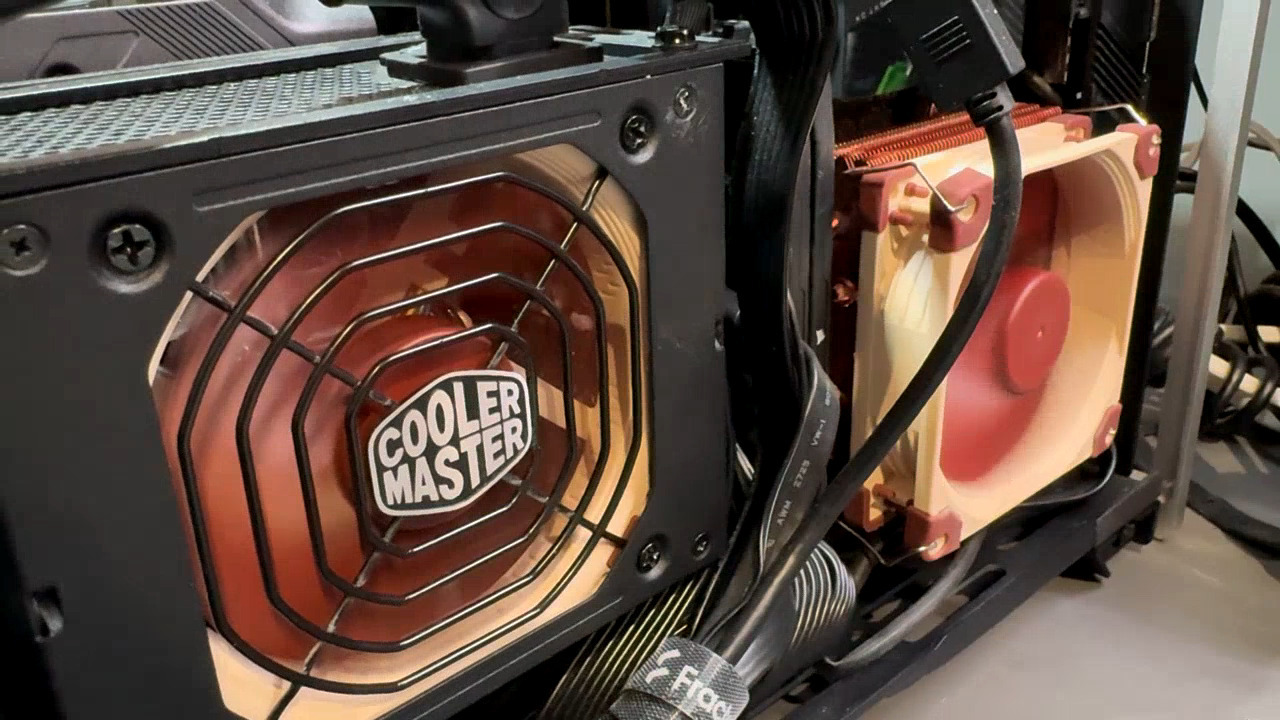 Computer with the side panel removed, with a Noctua fan visibly spinning inside the PSU, next to another Noctua fan spinning above the CPU.
