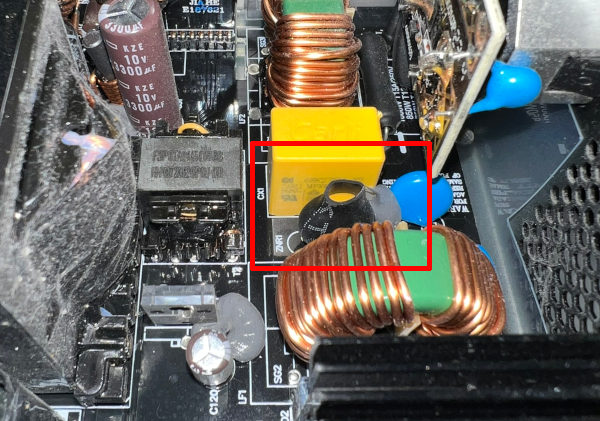 Inside of a computer PSU: a printed circuit board with various components on it. Highlighted is a component wrapped in heatshrink, with the label ZNR1 next to it.